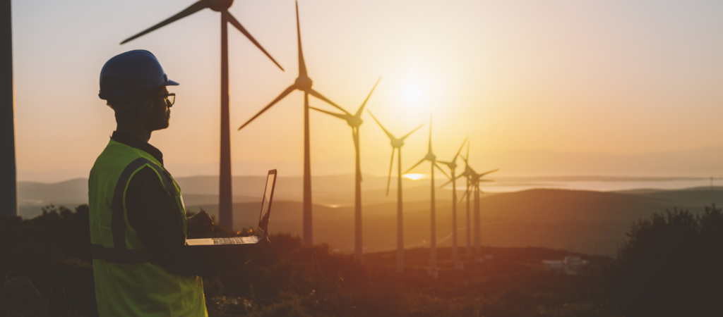 engineer stands in front of wind turbines in sunset